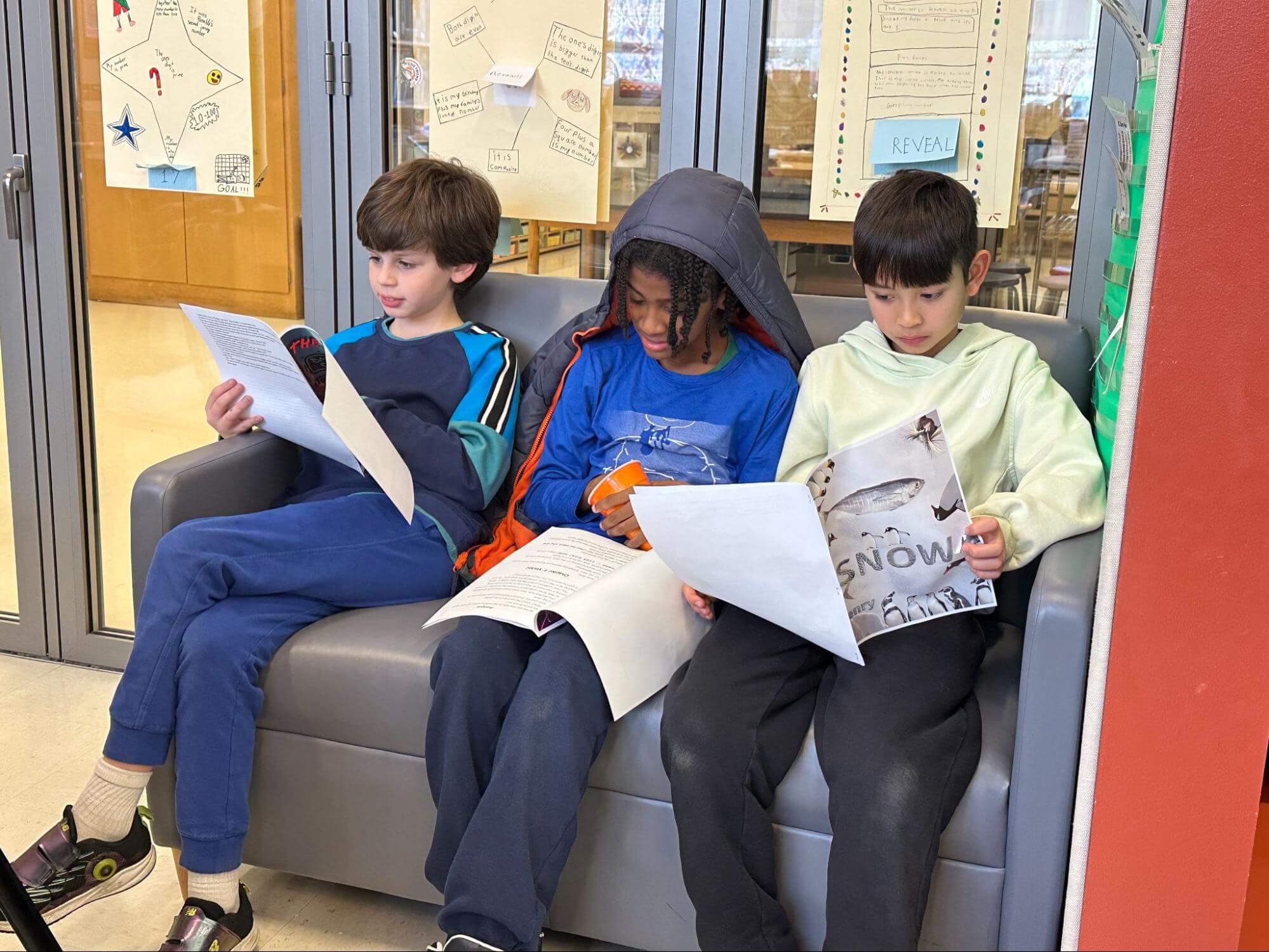 Three Ethical Culture Fieldston School Fieldston Lower students sit on a couch reading each other's stories during a publishing party.