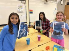 Three Ethical Culture Fieldston School Fieldston Lower students smile as they hold up their finished dystopian fiction stories.