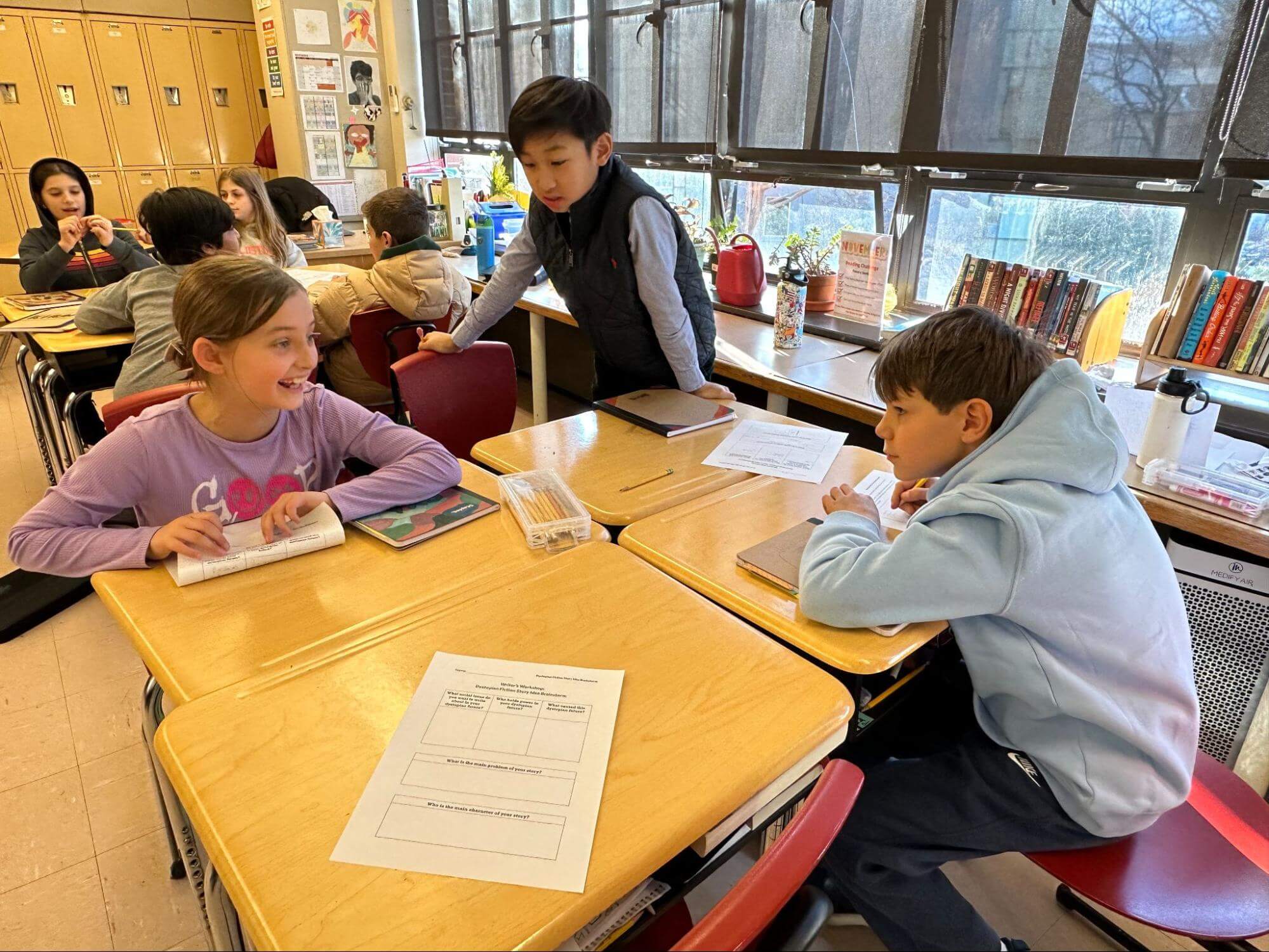 A group of Ethical Culture Fieldston School Fieldston Lower students gather around a table, having a discussion during a writing workshop.