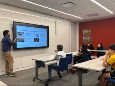 A group of Ethical Culture Fieldston School students sits at a table listening to a lesson on media literacy.