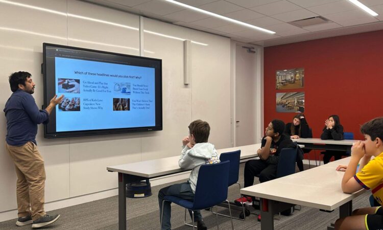 A group of Ethical Culture Fieldston School students sits at a table listening to a lesson on media literacy.