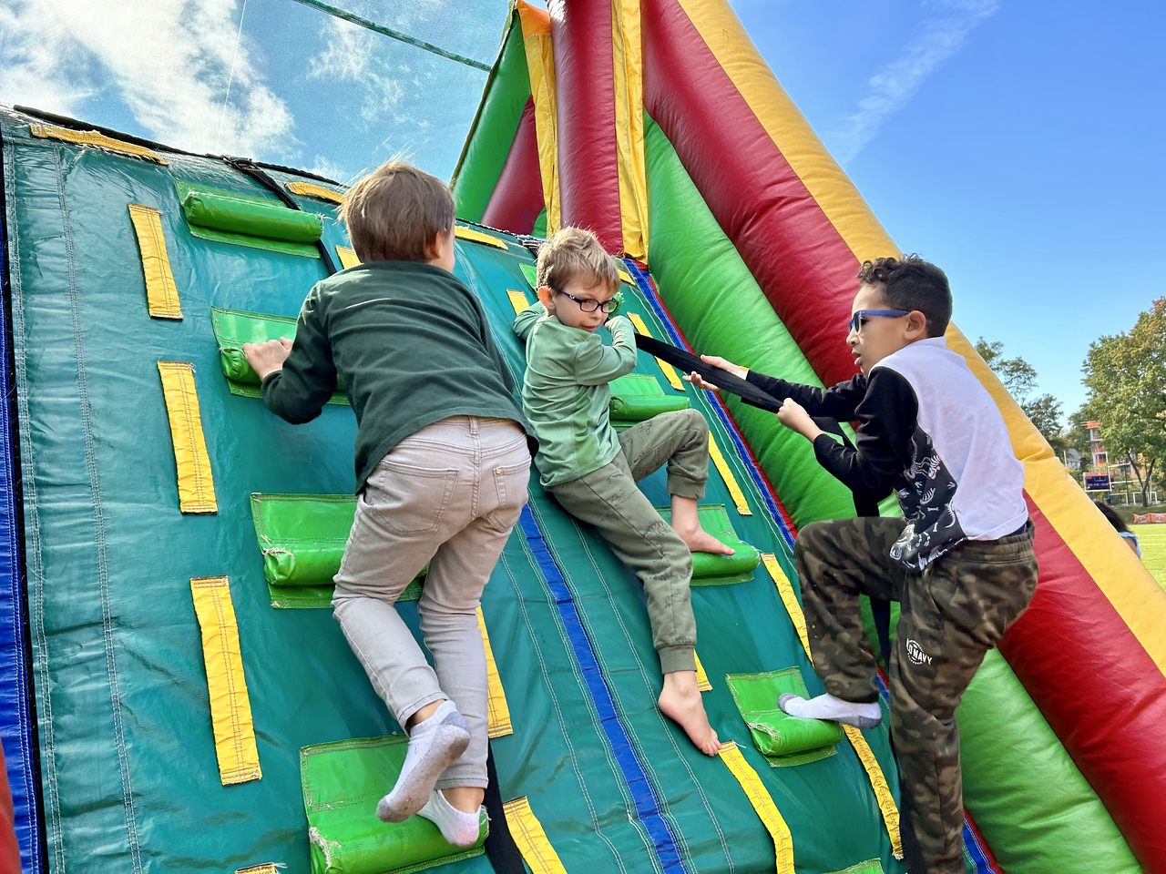 Three Fieldston Lower Students climb bouncy house at the Fall Carnival.