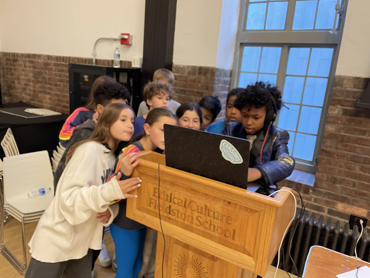 Fieldston Middle students gather at student social as one student uses computer to DJ.