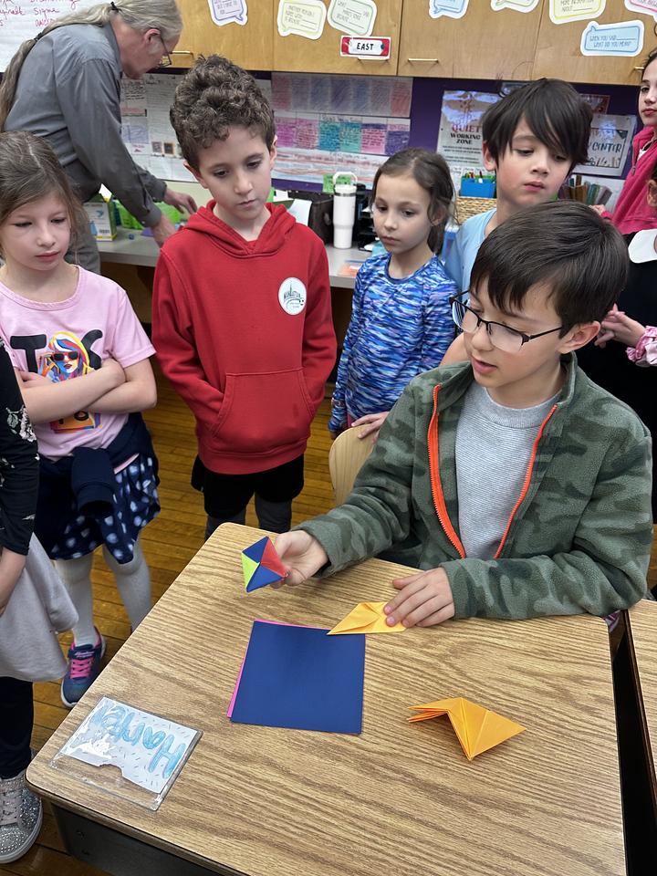 5th Grade student at Ethical Culture presents his math work to 2nd Grade onlookers in classroom.