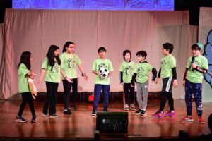 Ethical Culture students dressed in green perform onstage during 4th Grade play.