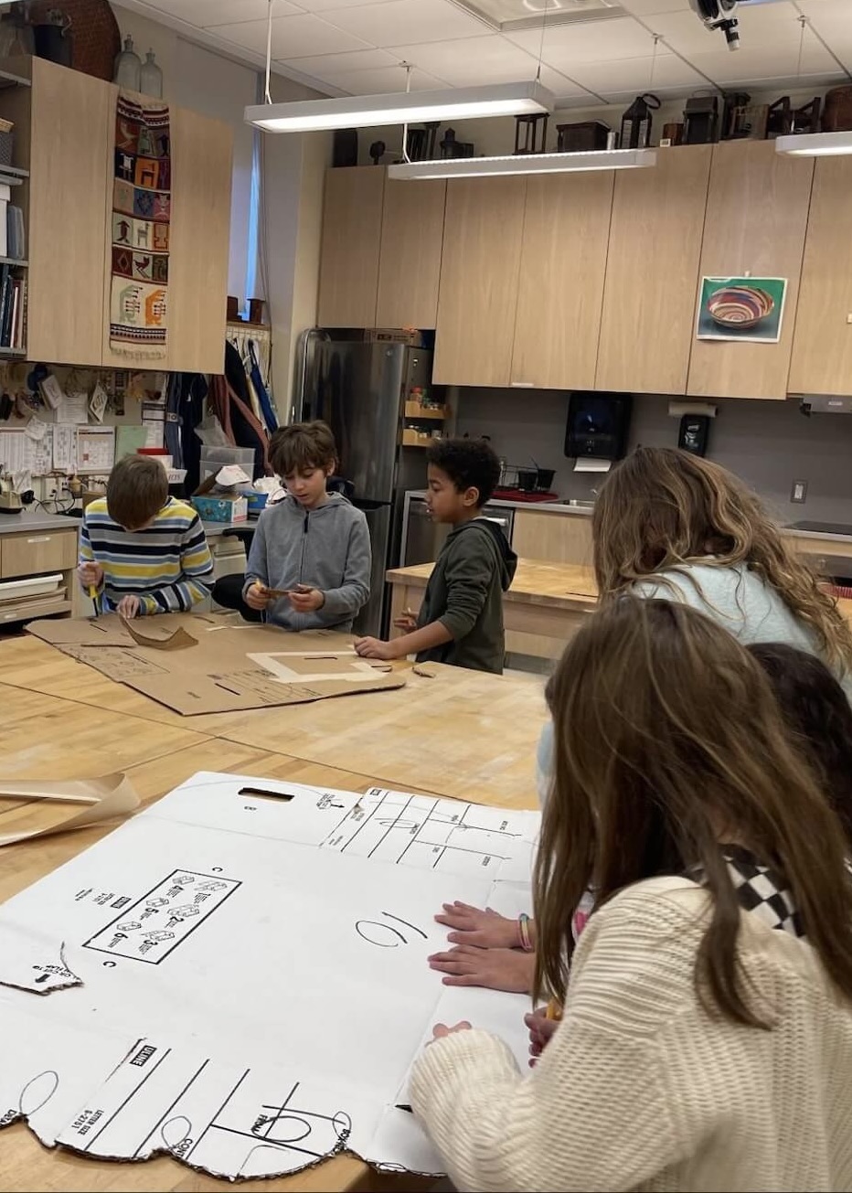 Fieldston Lower students sit at a table and build a set piece for the 3rd Grade musical.