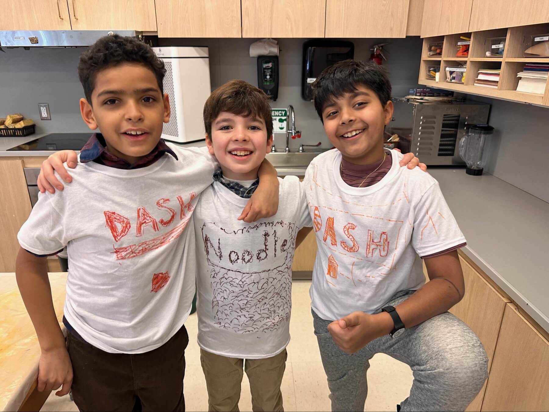 Three Fieldston Lower 3rd Graders stand with their arms around each other, showing off the costumes they designed for the musical.