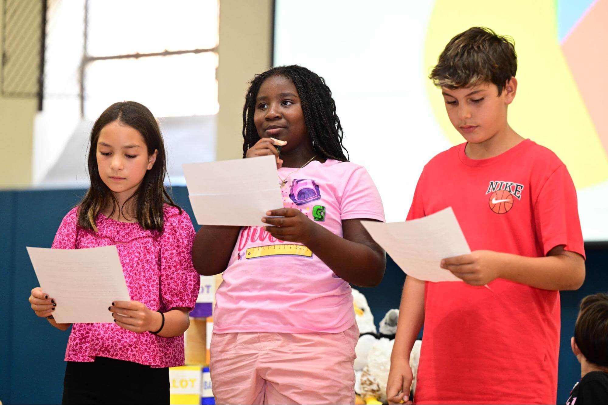 Three Ethical Culture Fieldston School Fieldston Lower students present at an assembly looking thoughtful.