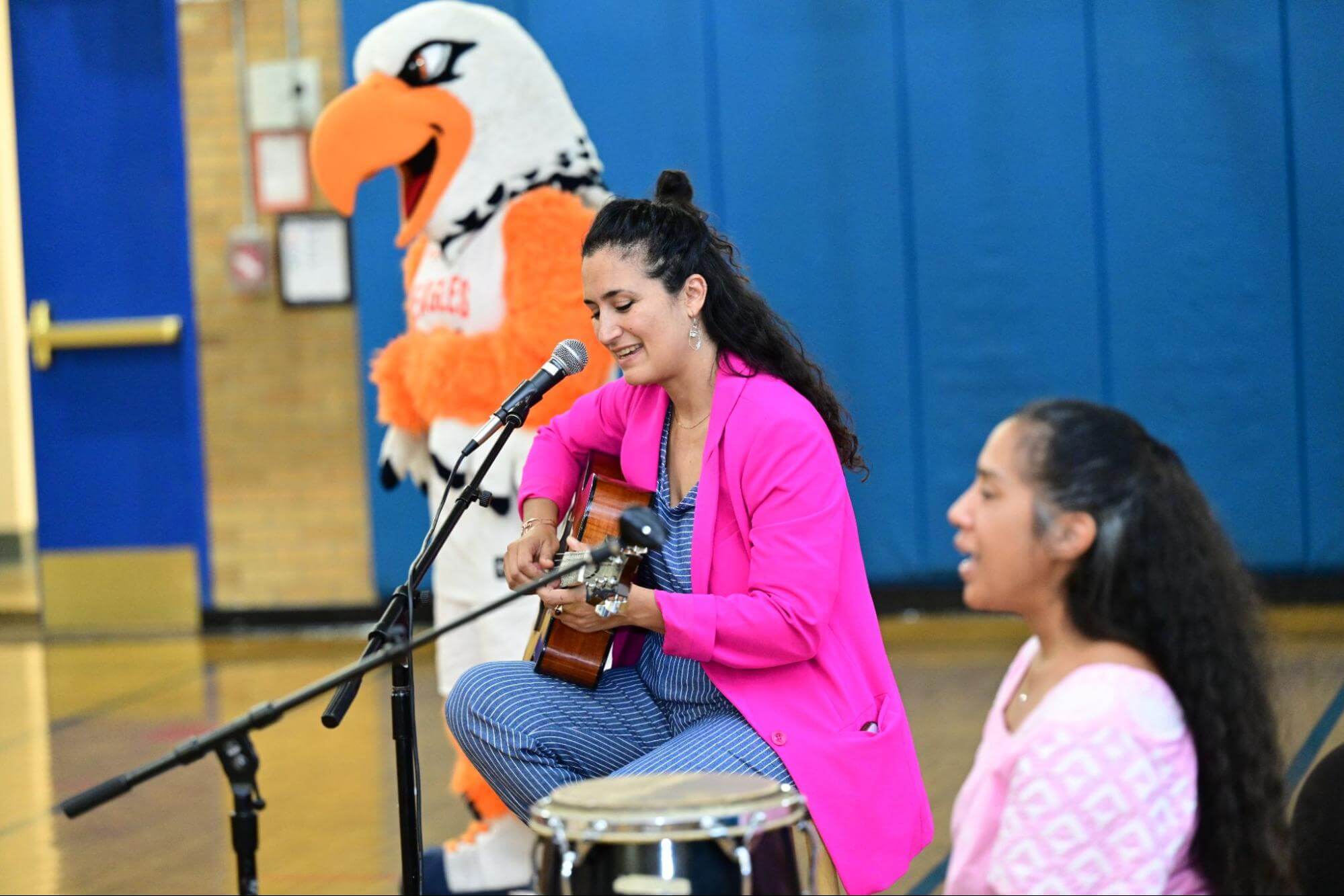 Ethical Culture Fieldston School's mascot and two Fieldston Lower School teachers sing a song and play guitar at an assembly.