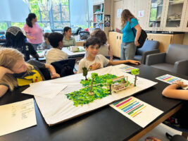 Fieldston Lower student smiles with Shark Tank project model outdoor classroom.