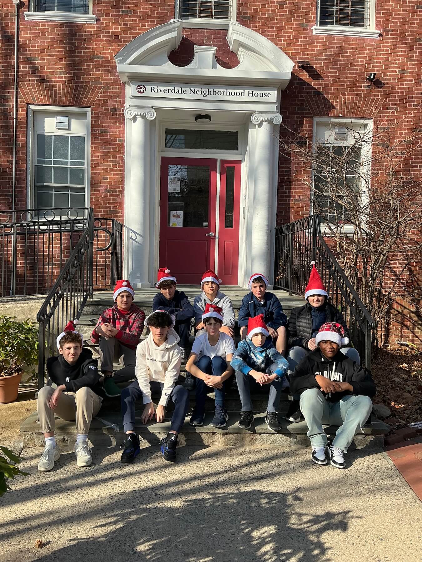 The members of Ethical Culture Fieldston School's 7th Grade Boys Chorus pose in front of a building sitting down wearing festive clothes.