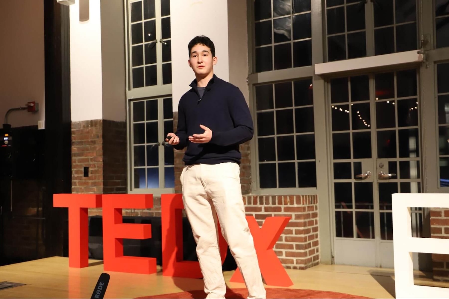 An Ethical Culture Fieldston school senior stands and speaks at the TEDxECFS event. He is gesturing calmly as if to emphasize an important point.