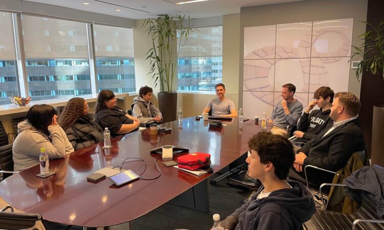 A group of six Ethical Culture Fieldston School students sit at a table at an investment firm