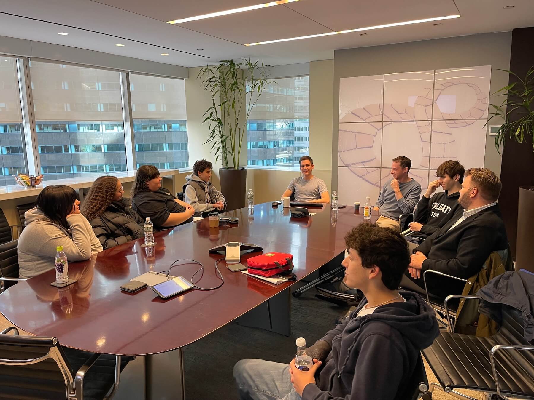 A group of six Ethical Culture Fieldston School students sit at a table with private equity investors and CEO Kyle Wilkie-Glass