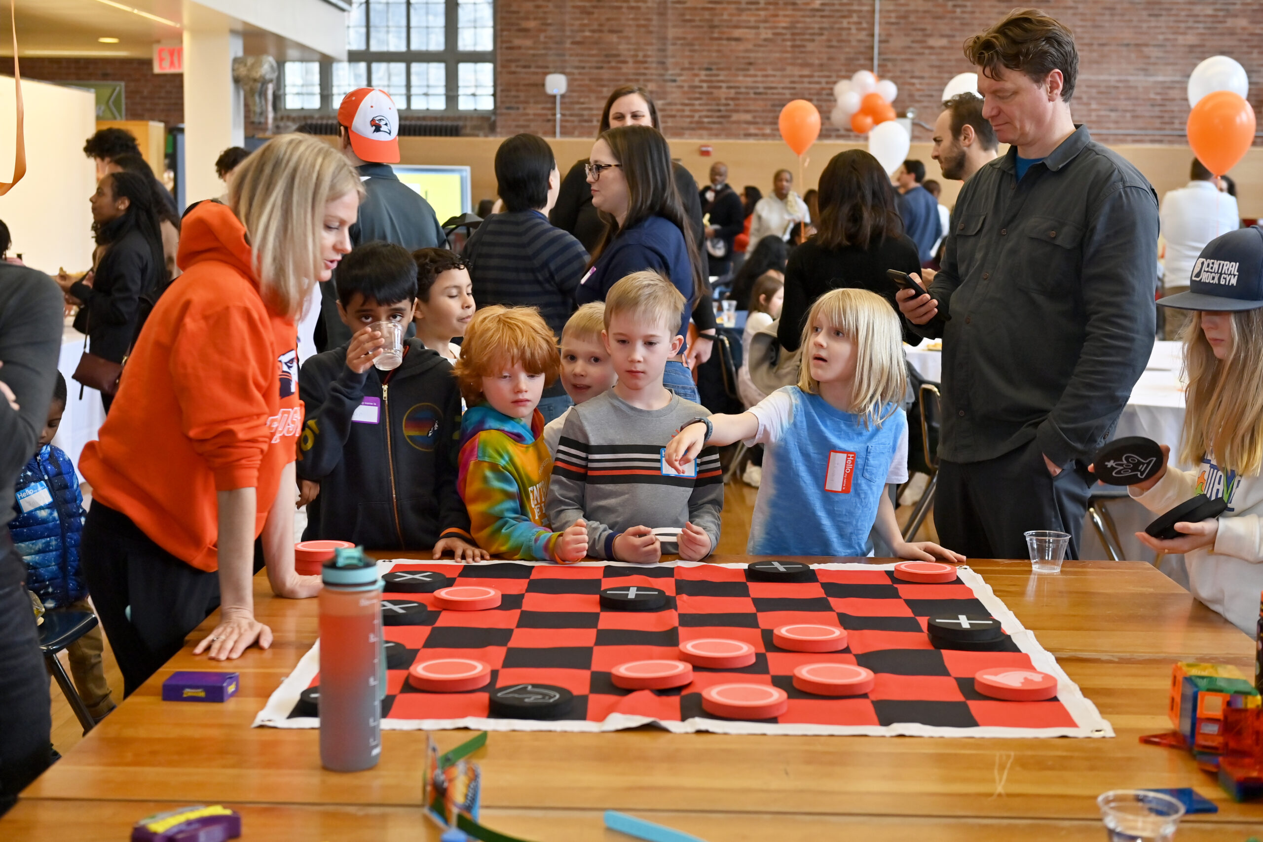 A group of students plays with a giant checkerboard as two adults watch